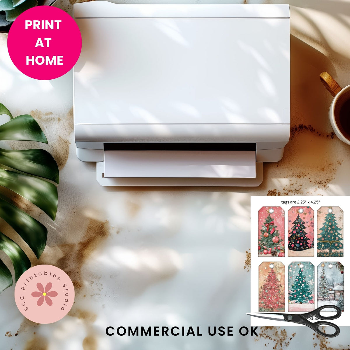A white rectangular printer or label printer shown from above on a marble-like surface with shadows, alongside a pink 'PRINT AT HOME' badge, a pink 'SCC Printables Studio' logo, 'COMMERCIAL USE OK' text, scissors, and a small inset showing Christmas tree print options.