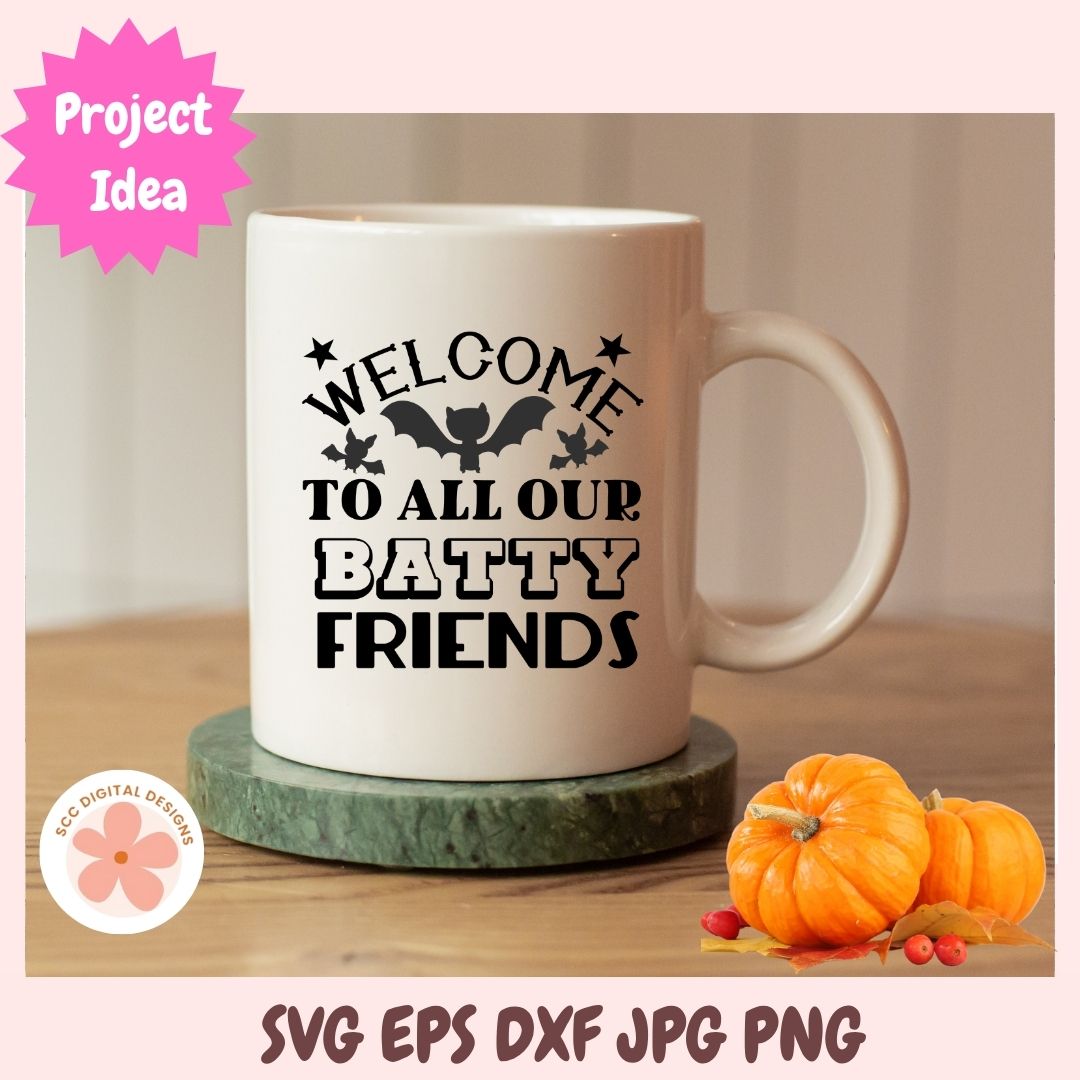 White mug with 'Welcome to all our batty friends' text on a wooden surface with pumpkins.