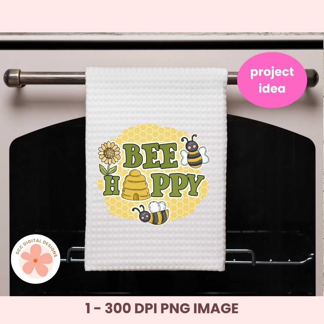 White towel with bee-themed design hanging on an oven rack, featuring the text 'BEE HAPPY'.