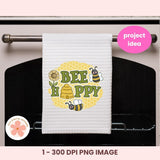 White towel with bee-themed design hanging on an oven rack, featuring the text 'BEE HAPPY'.