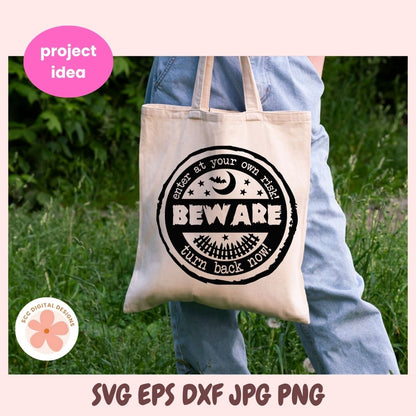 Person holding a tote bag with a 'Beware' design in a grassy outdoor setting