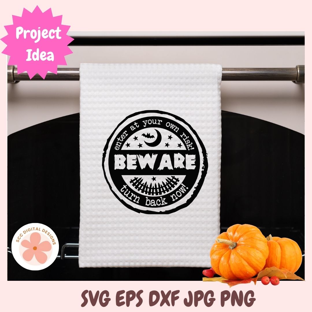 White towel with 'Beware' design hanging on a rack, with pumpkins and decorative elements below.