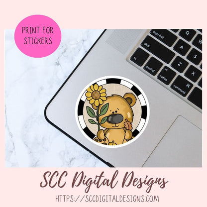 A circular sticker design featuring a cute cartoon bear holding a yellow sunflower, shown placed on a silver laptop. The image includes a pink circle that says 'PRINT FOR STICKERS' and text at the bottom reading 'SCC Digital Designs' with a website URL.