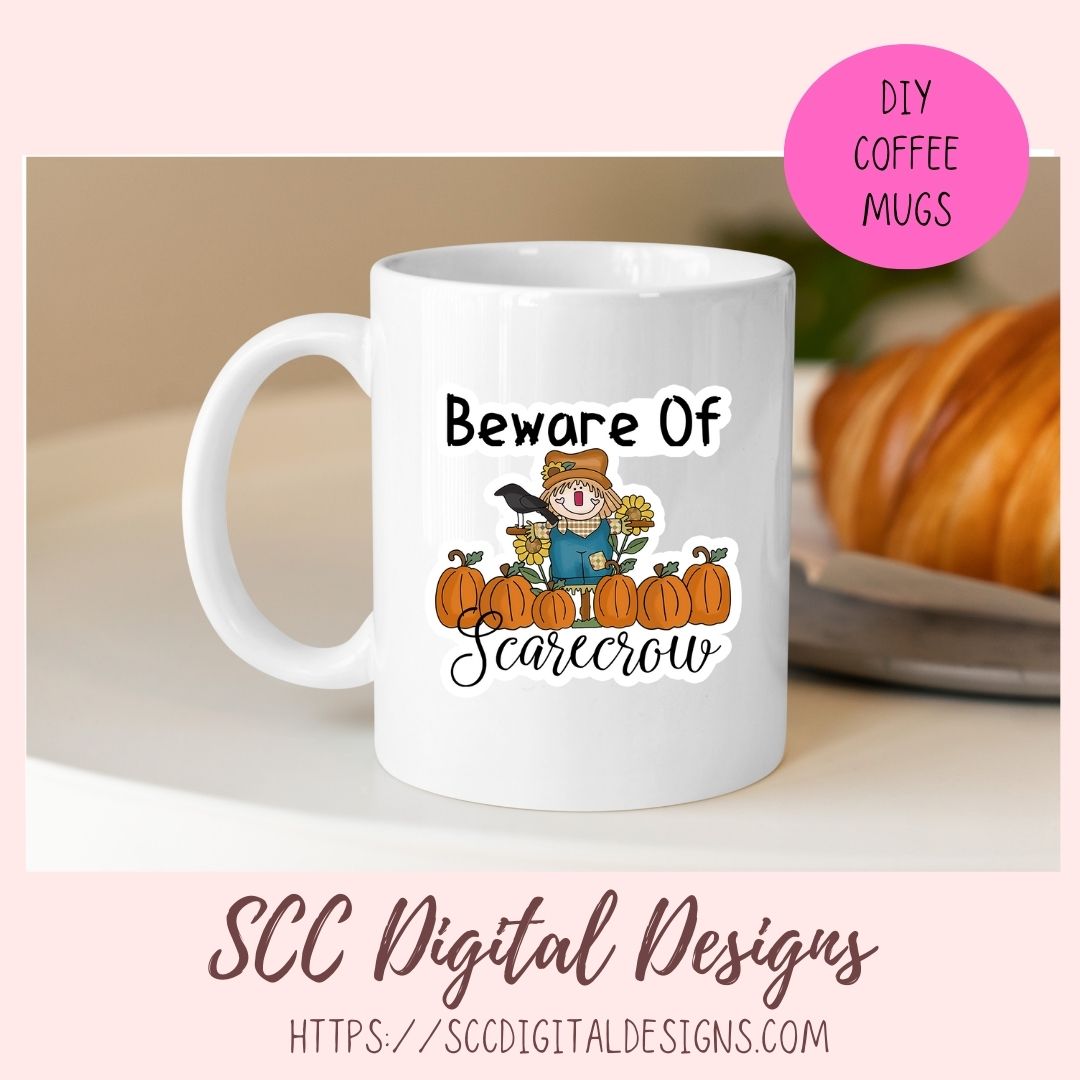 A white ceramic coffee mug with a 'Beware of Scarecrow' autumn graphic, shown in a styled mockup setting with a pink 'DIY COFFEE MUGS' badge and 'SCC Digital Designs' branding.