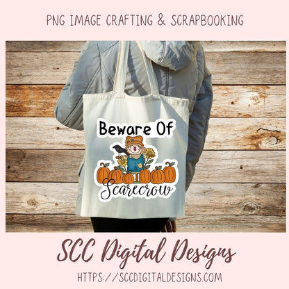 A person wearing a gray puffer jacket carries a canvas tote bag with a fall-themed graphic that reads 'Beware Of Scarecrow' above an illustration of pumpkins, a scarecrow, and a bird. The photo is framed with a pale pink border and text reading 'PNG IMAGE CRAFTING & SCRAPBOOKING' at the top and 'SCC Digital Designs' at the bottom.