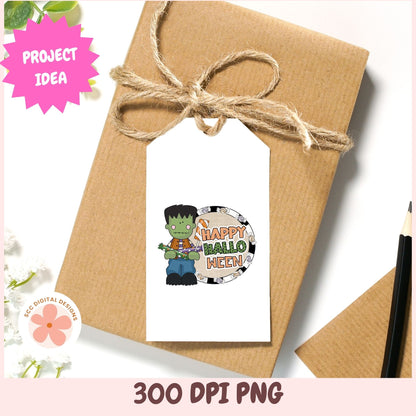 A kraft paper gift box tied with twine and a white gift tag featuring a Halloween Frankenstein graphic that reads 'Happy Halloween' in colorful lettering. The image includes decorative pink and white corner graphics and text reading '300 DPI PNG' and 'Project Idea'.