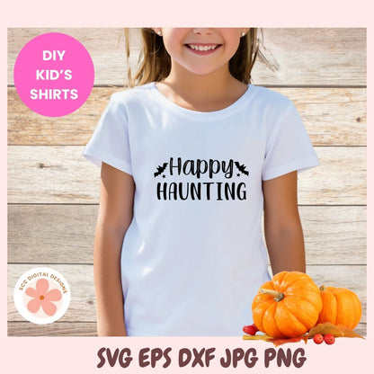 Child wearing a white t-shirt with '#Happy Haunting' text, surrounded by pumpkins on a wooden background.