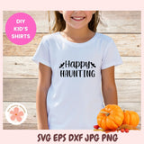 Child wearing a white t-shirt with '#Happy Haunting' text, surrounded by pumpkins on a wooden background.