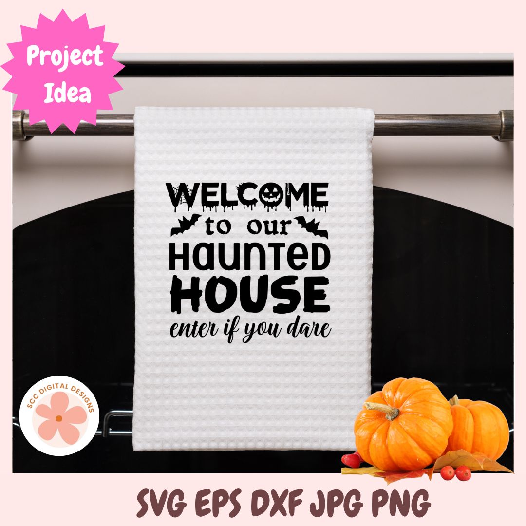 A white waffle-knit kitchen towel hanging on a metal rack, printed with the phrase 'WELCOME to our HAUNTED HOUSE enter if you dare' in black text with small bat and skull motifs. The image includes decorative pumpkins at the bottom right, a pink 'Project Idea' badge at top left, and file-format text at the bottom.
