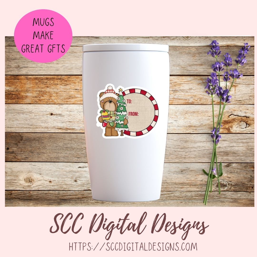 A white insulated tumbler with a lid is centered on a rustic wood plank background, decorated with a Christmas-themed sticker showing a teddy bear and a candy cane. A pink circular badge in the top left reads 'MUGS MAKE GREAT GFTS', and purple lavender stems sit to the right.