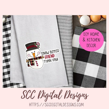 A digital design mockup for a kitchen towel featuring a snowman wearing a black and red plaid top hat and scarf, with the text 'SNOWY BETTER FRIEND THAN YOU!' on a light gray towel. The image includes a pink circular badge reading 'DIY HOME & KITCHEN DECOR' and a bottom banner for 'SCC Digital Designs'.