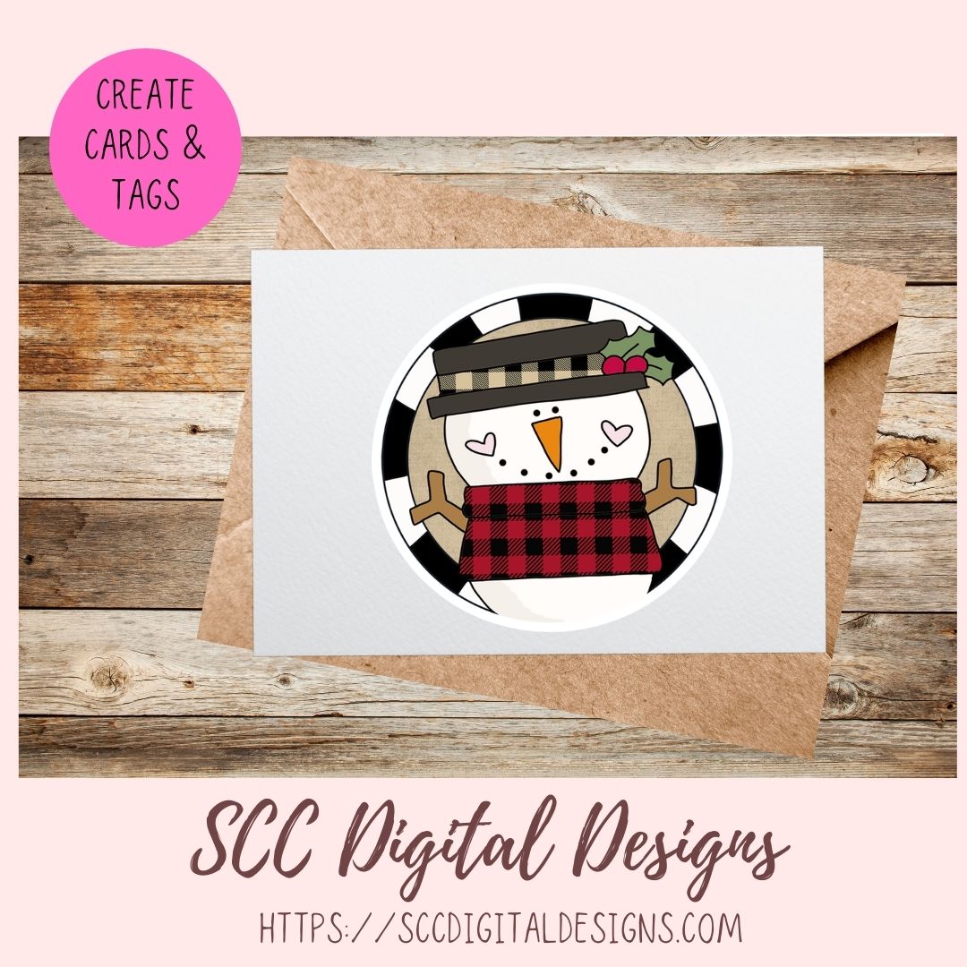 A square white card featuring a circular snowman illustration with a black-and-white plaid hat and red plaid scarf, shown on top of a kraft envelope over a rustic wood background. A pink circle in the upper left says 'CREATE CARDS & TAGS,' and text at the bottom reads 'SCC Digital Designs' with a website.