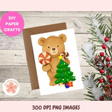 Card with a bear holding a candy cane and Christmas tree, surrounded by festive decorations on a wooden surface.