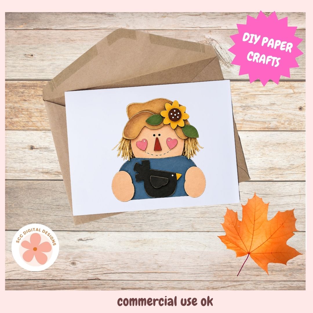 A white greeting card featuring a cute cartoon scarecrow with a yellow flower on its hat, shown partially tucked into a brown kraft envelope on a wood plank background. Pink promotional badges read 'DIY PAPER CRAFTS' and 'commercial use ok', with a small 'Eco Digital Designs' logo in the lower left.