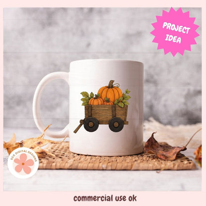 A white ceramic mug with a fall harvest graphic of pumpkins in a wooden wagon, styled on a woven placemat with autumn leaves against a gray wood background. The image features a pink 'PROJECT IDEA' starburst and a 'commercial use ok' label.