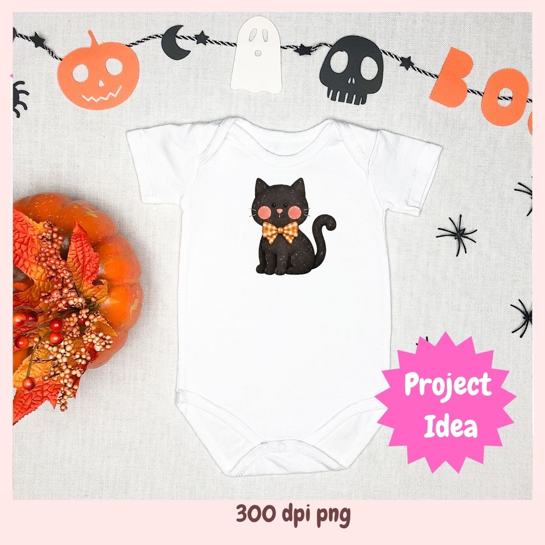 A white short-sleeve baby bodysuit laid flat on a light fabric background, featuring a black cat illustration with pink cheeks and a gold bow tie. Halloween-themed props including a pumpkin, spider, moon, ghost, skull, and orange garland surround the bodysuit.