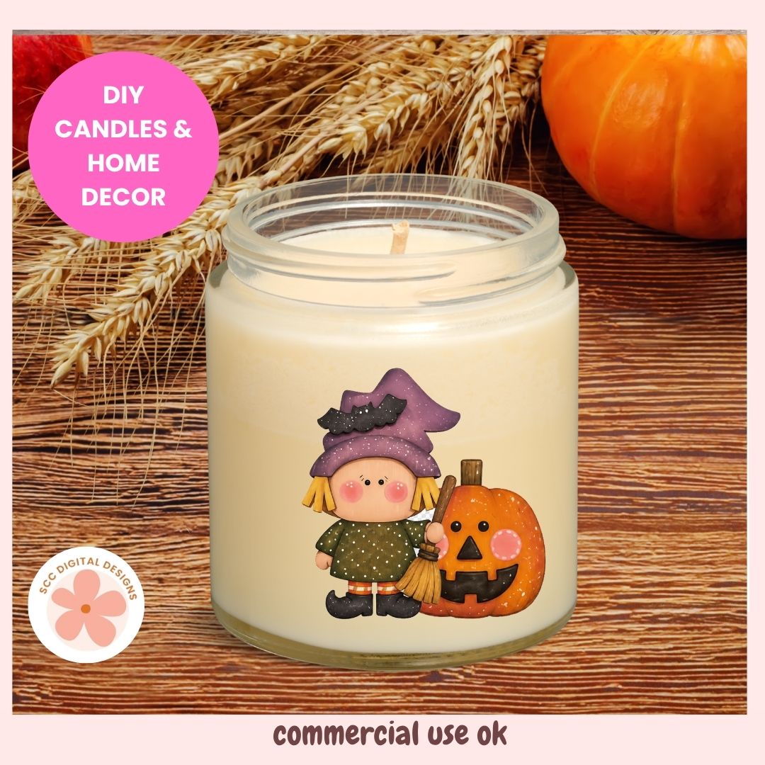 A jar candle with a Halloween-themed illustration of a witch and a jack-o'-lantern on the front. The candle is set on a rustic wooden surface with decorative wheat stalks and a pumpkin in the background.