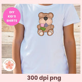 White t-shirt with a bear design holding flowers, on a wooden surface.