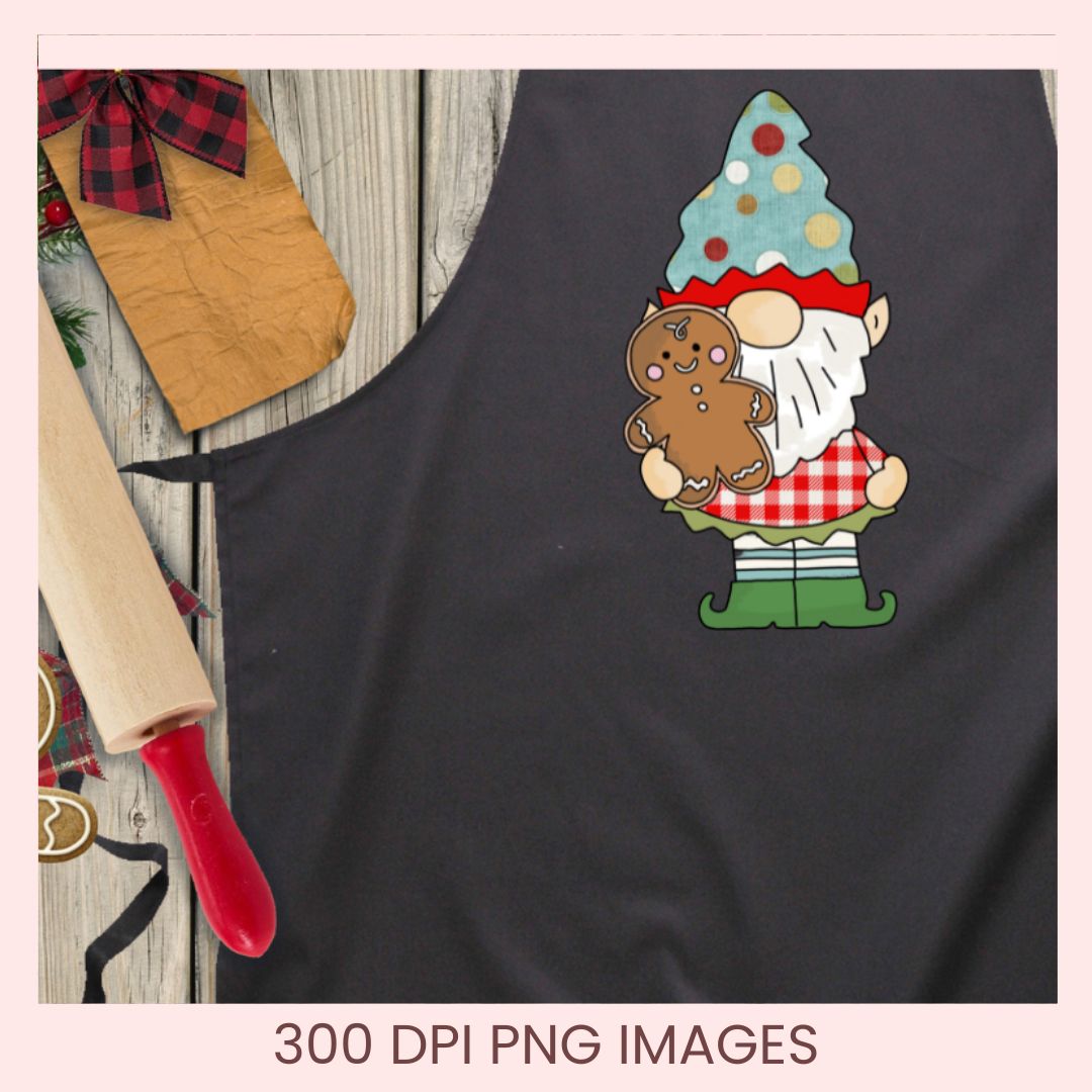 A dark charcoal gray apron laid flat on a rustic wood surface with holiday styling props, including a wooden rolling pin, a brown paper tag with a red plaid bow, and gingerbread cookie decorations. The apron has a colorful gnome graphic on the chest holding a gingerbread man.
