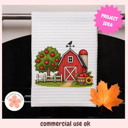 A white waffle-weave kitchen towel featuring a colorful autumn farm illustration with a red barn, apple tree, silo, and sunflower. The towel hangs on a dark oven door, with decorative pink 'PROJECT IDEA' and 'commercial use ok' text overlays.
