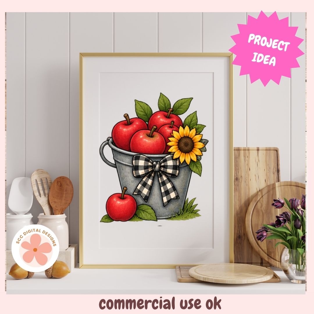 Framed wall art featuring an illustration of red apples, green leaves, a yellow sunflower, and a gray bucket with a black-and-white checkered bow, displayed in a styled kitchen setting with a pink 'PROJECT IDEA' badge and 'commercial use ok' text.