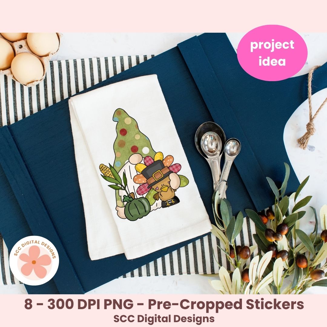 A styled flat-lay showing a white fabric napkin with a colorful Thanksgiving-themed gnome illustration, placed on navy blue paper with measuring cups, eggs, and olive branches around it. Pink text badges read 'project idea' and '8 - 300 DPI PNG - Pre-Cropped Stickers' with 'SCC Digital Designs' at the bottom, indicating this is a digital design preview rather than a straightforward physical product photo.