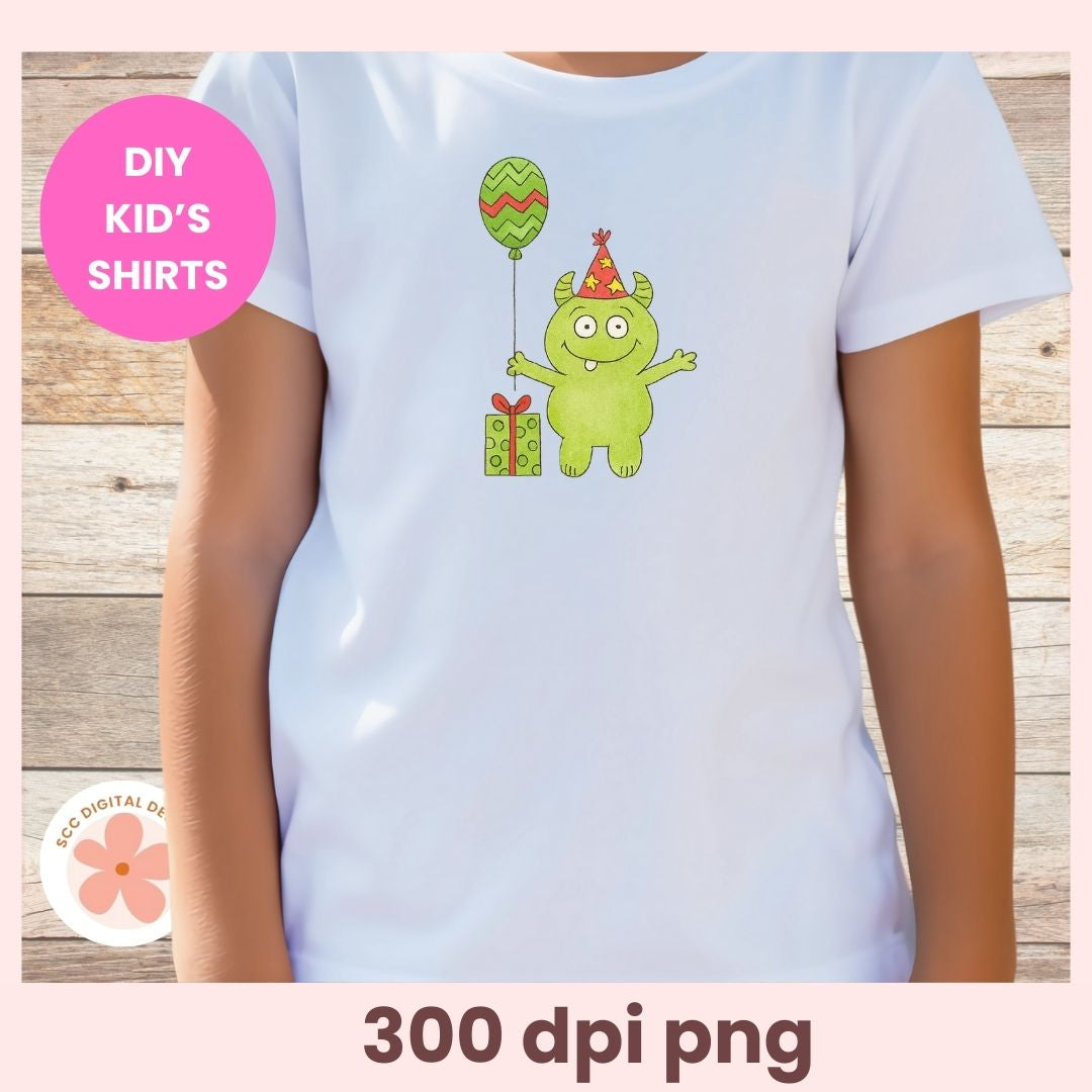 White t-shirt with a green monster design holding a balloon and gift, on a wooden surface.