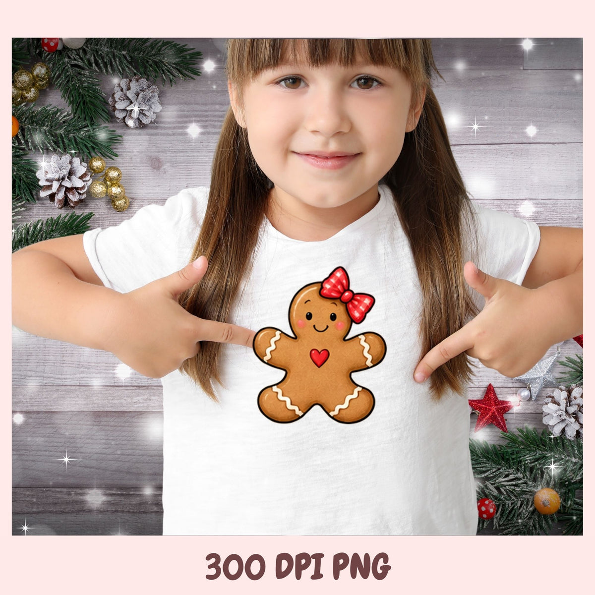 A young girl with brown hair in pigtails points at a graphic design on her white t-shirt. The graphic shows a gingerbread man with a red bow and heart.