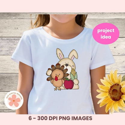 A child wearing a white short-sleeve T-shirt with a cartoon Thanksgiving-themed bunny and turkey graphic on the front, shown against a rustic wood background with a pink 'project idea' badge and a sunflower decoration.