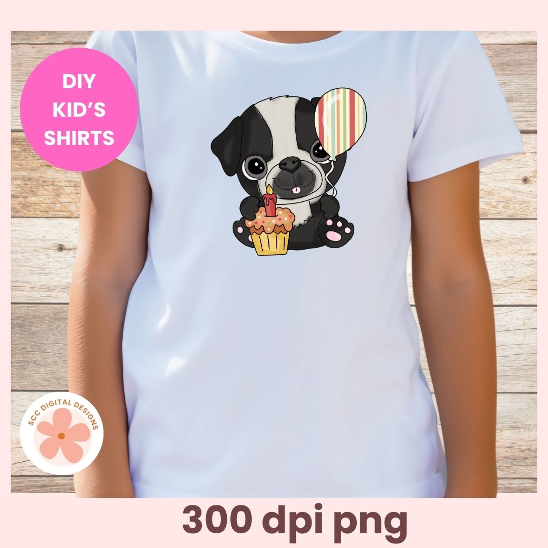 White t-shirt with a cartoon dog holding a cupcake and candle, on a wooden surface.
