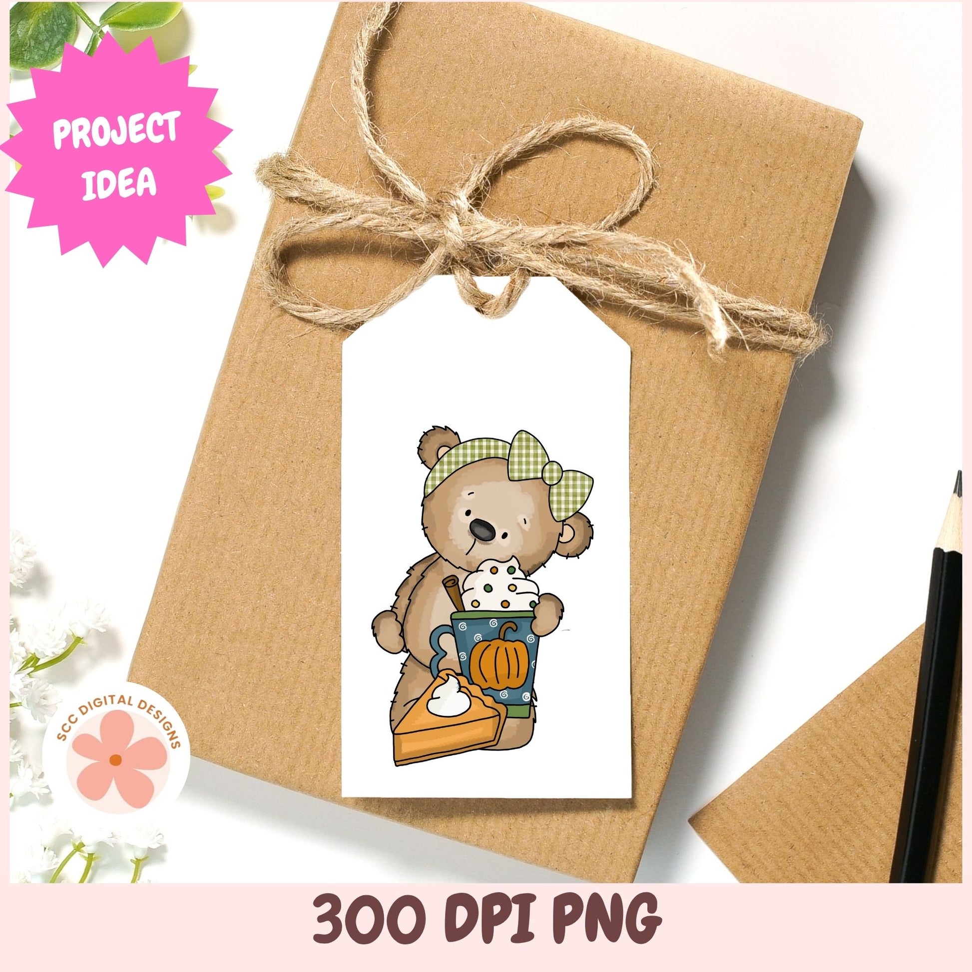 A styled flat-lay mockup of a kraft paper gift box tied with twine and a white gift tag featuring a cartoon teddy bear holding a pumpkin and a cup. Decorative pink and white graphics, including the text 'PROJECT IDEA' and '300 DPI PNG', frame the image.