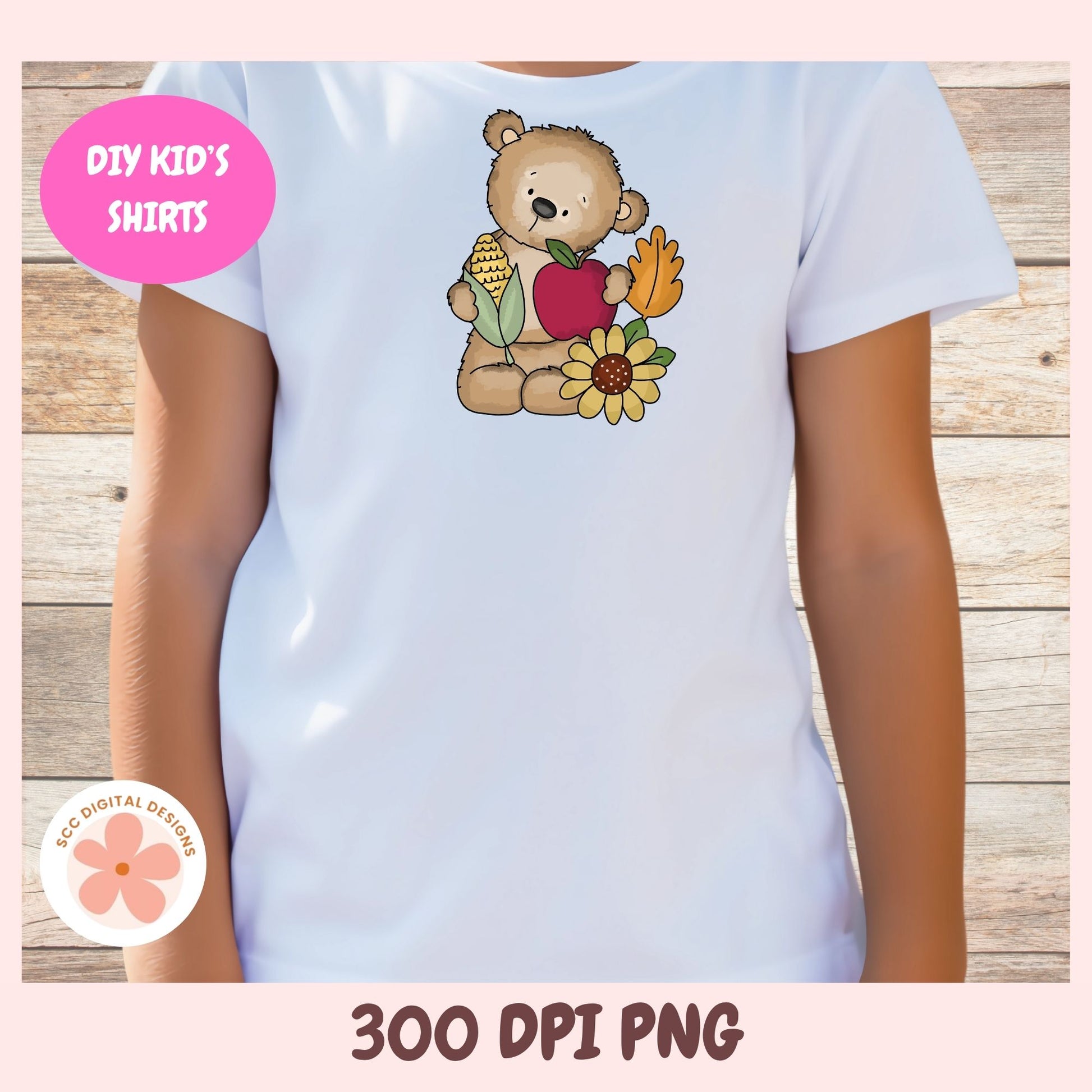 A child wearing a white short-sleeve T-shirt with a cartoon teddy bear holding a red apple, corn, and a yellow flower, shown against a wood plank background. Pink promotional badges read 'DIY KID'S SHIRTS' and '300 DPI PNG'; a circular logo says 'SECO DIGITAL DESIGNS'.