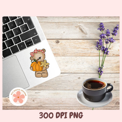 A digital sticker design of a cute autumn bear holding a pumpkin and a star, shown applied to a laptop sticker. The scene is styled on a rustic wooden background with a laptop, a cup of coffee, and purple lavender flowers, framed by a pink border with '300 DPI PNG' text at the bottom.