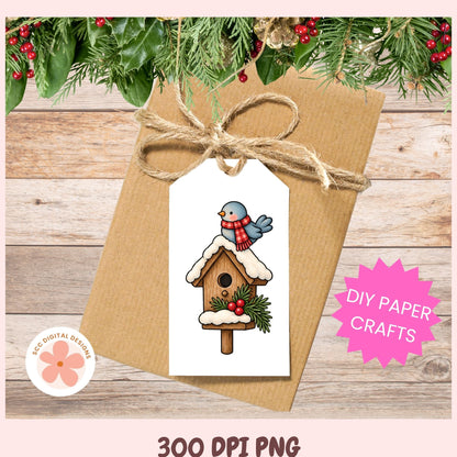 A kraft paper gift tag with a white hanging label featuring a winter birdhouse illustration with a blue bird and red scarf, tied with twine on a brown kraft envelope. The scene is styled with pine branches and red berries, with text reading 'DIY PAPER CRAFTS' and '300 DPI PNG'.