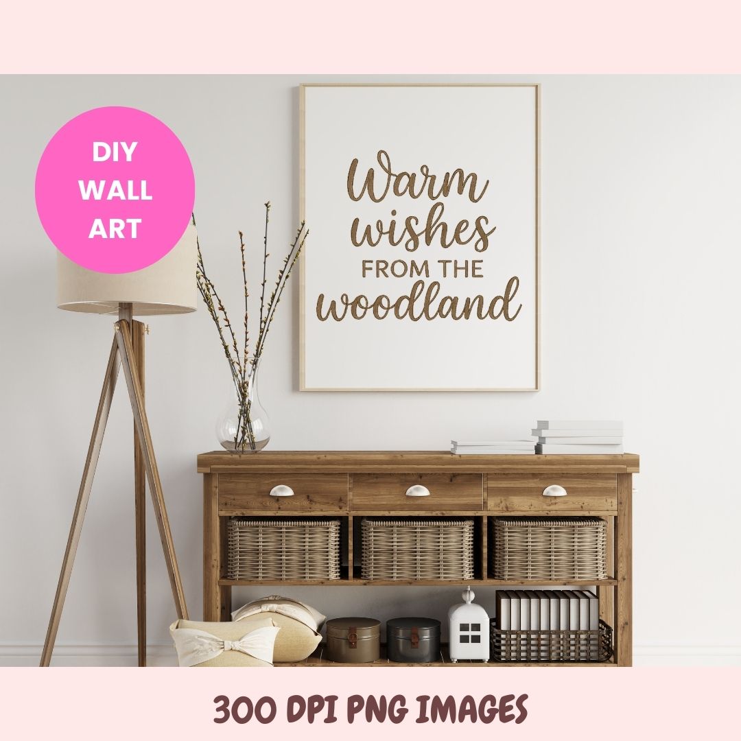 A framed typographic wall art print reading 'Warm wishes FROM THE woodland' in brown lettering on a white background, shown hanging above a wooden console table in a styled room. A pink circular badge says 'DIY WALL ART,' and text at the bottom says '300 DPI PNG IMAGES.