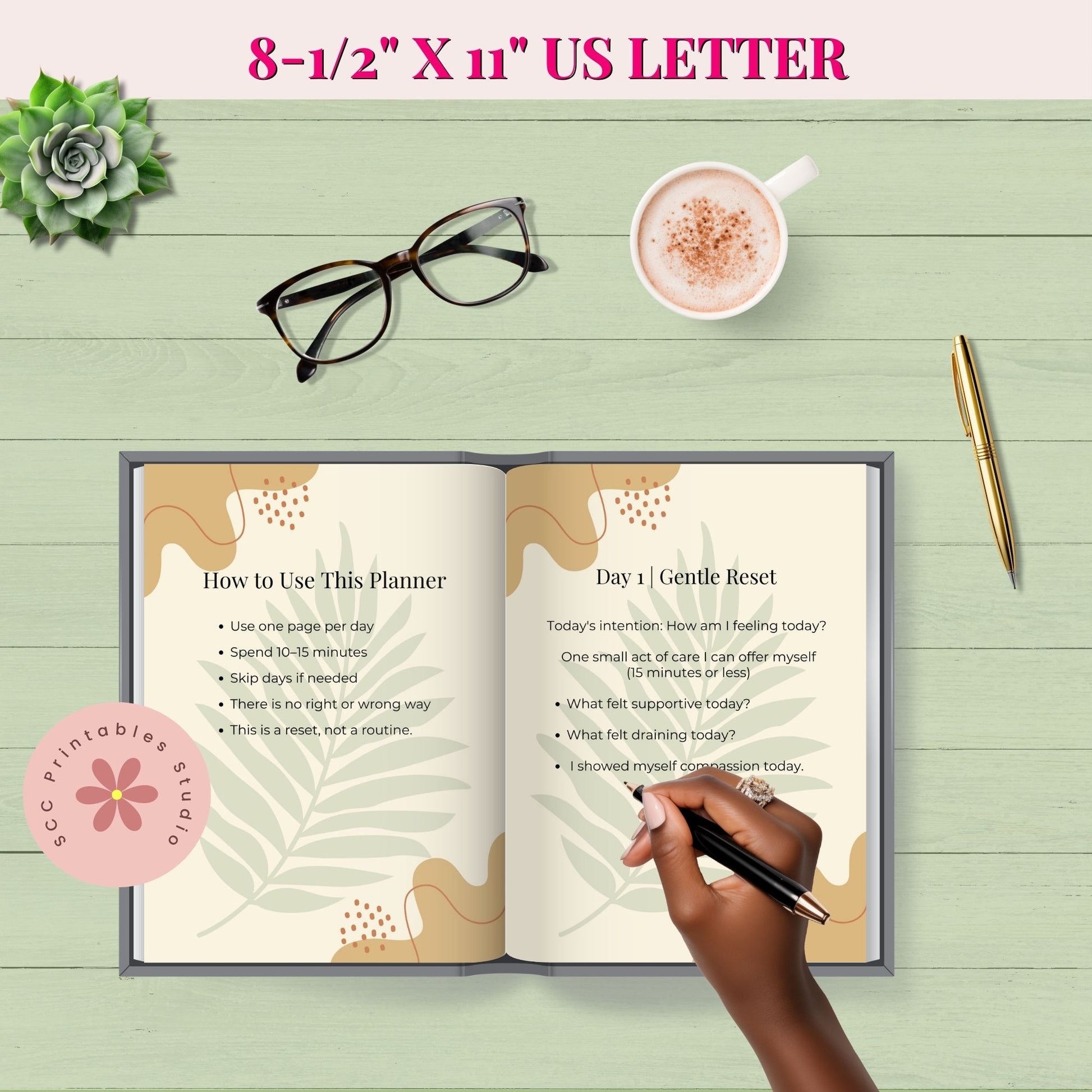 Open planner on a wooden surface with a hand holding a pen, a cup of coffee, glasses, and a succulent plant.