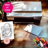Printer on a table with a coloring page of a Santa Claus figure, crayons, and a 'Print at Home' label.