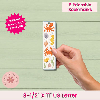 Hand holding a printed bookmark with sea-themed illustrations on a wooden surface.