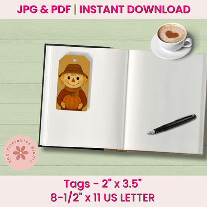 A printable autumn-themed tag design shown on an open notebook with a coffee cup and pen on a light wood background. The tag features a smiling scarecrow holding a pumpkin.