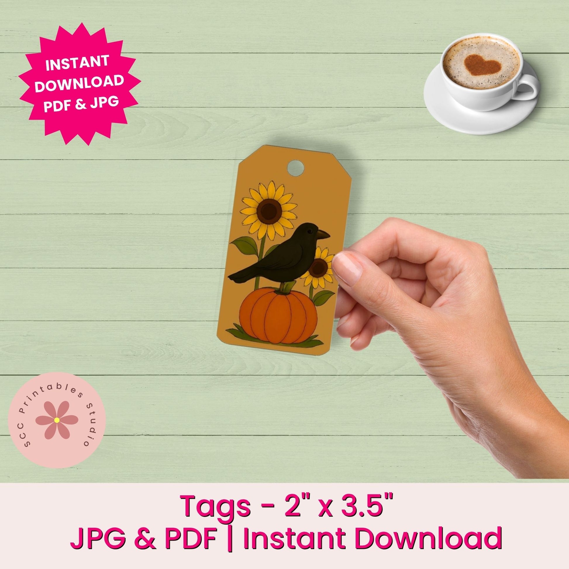 A hand holds a printed autumn-themed gift tag featuring a black bird on an orange pumpkin with sunflowers, shown over a light green wood background. Promotional text reads 'Instant Download PDF & JPG' and 'Tags - 2" x 3.