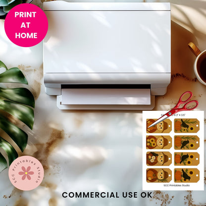 A white printer shown from above on a marble-like surface with a pink 'PRINT AT HOME' badge, a cup of coffee, green leaves, scissors, and a printed sheet of decorative tags. Text at the bottom reads 'COMMERCIAL USE OK' and 'SCC Printables Studio' appears on the print sheet.
