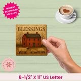 Hand holding a print with a house and sheep design, next to a cup of coffee on a wooden surface.