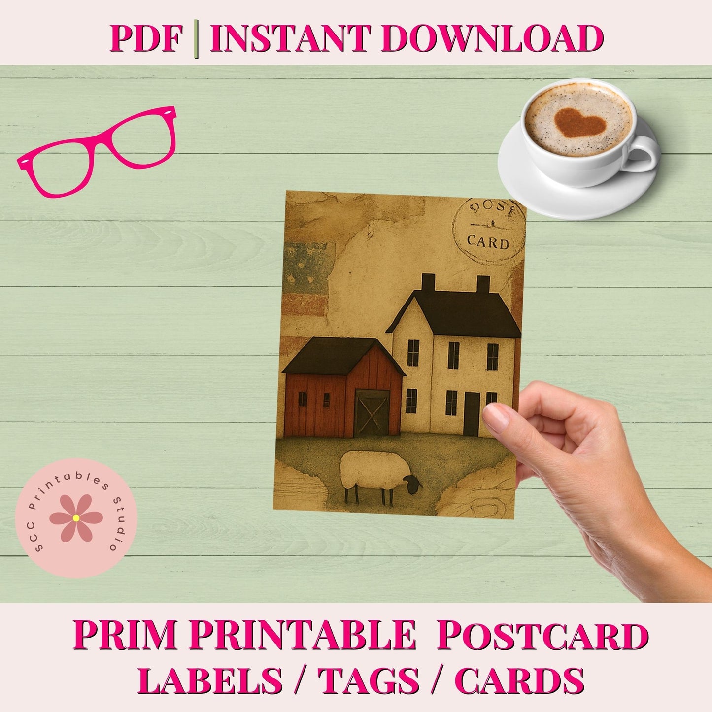 Hand holding a postcard with houses and sheep, with a cup of coffee and glasses on a wooden surface.