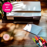 Printer on a wooden surface with colorful crayons and a 'Print at Home' label.