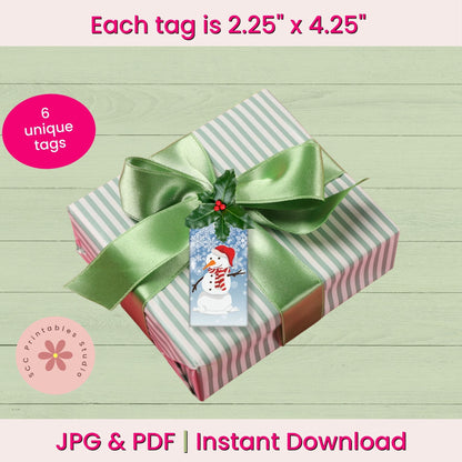 A wrapped gift box with a green satin ribbon and a snowman-themed printable gift tag, shown on a pale wood background with text reading 'Each tag is 2.25" x 4.25"
