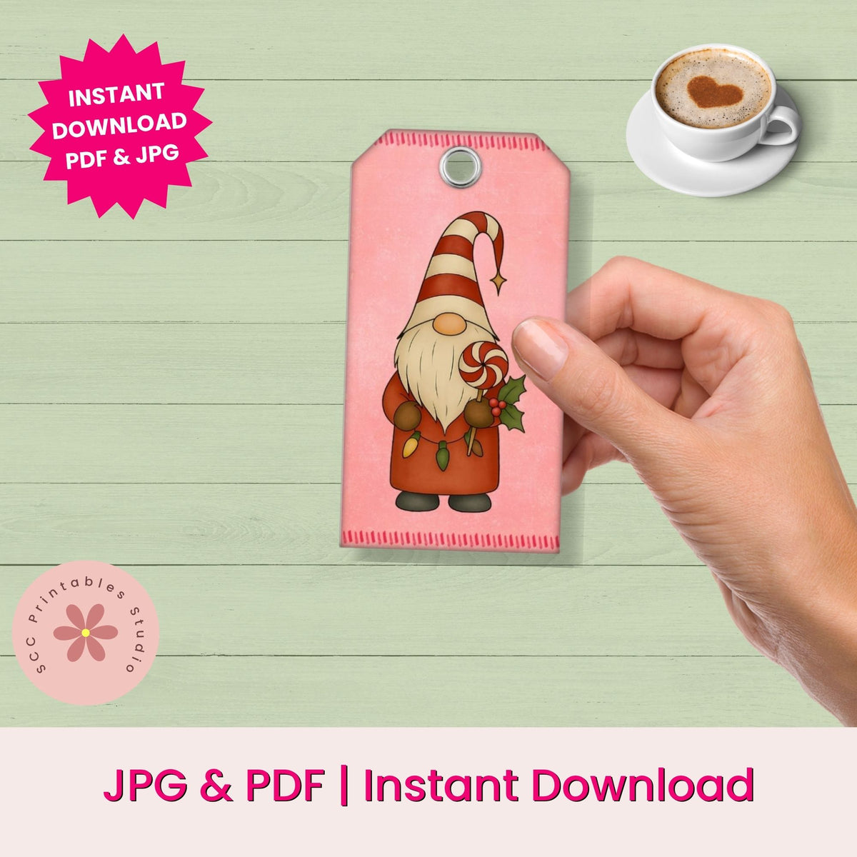 A hand holds a pink printable gift tag featuring a gnome illustration, with text reading 'INSTANT DOWNLOAD PDF & JPG' and 'JPG & PDF | Instant Download Download' on a light wood background.