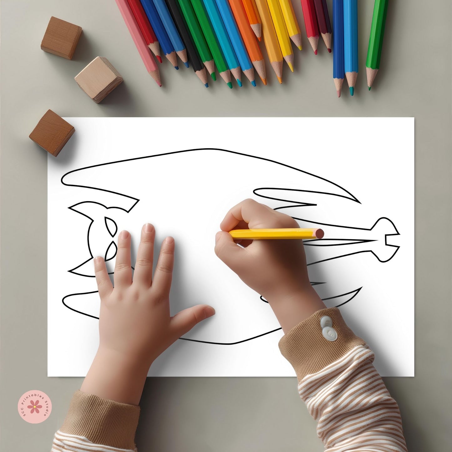 Child coloring a fish outline with colored pencils on a gray surface