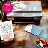Printer on a table with coloring book pages and crayons, featuring 'Print at Home' text.