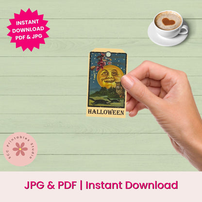 A hand holds a small tarot-style Halloween card featuring a smiling moon face, bats, and the word HALLOWEEN. The background is a pale green wood plank surface with promotional text reading 'INSTANT DOWNLOAD PDF & JPG' and 'JPG & PDF | Instant Download.