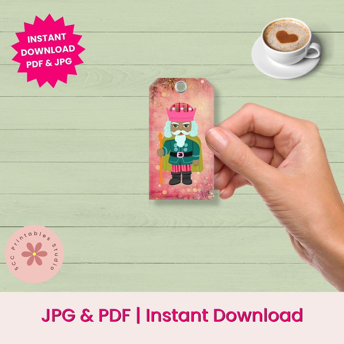 A hand holds a small printed card featuring a colorful nutcracker illustration against a light green wood background. The image includes promotional text reading 'Instant Download PDF & JPG' and 'JPG & PDF | Instant Download', plus a cup of coffee with a heart-shaped latte art design in the top right.